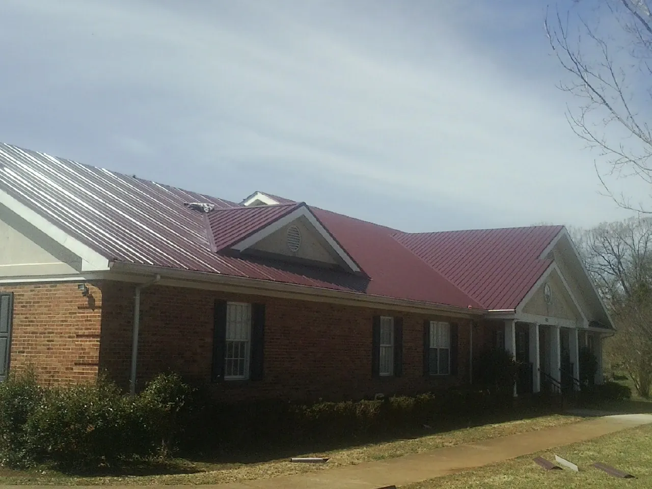 Red metal roof with gabled entries on a long brick building, from a Hail Damage Roof Repair job in Mount Braddock
