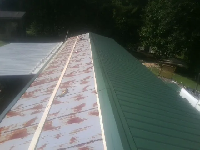 Old rusted panels beside newly installed green metal roofing — Wind Damage Roof Repair by Roofing Brothers in Mount Braddock