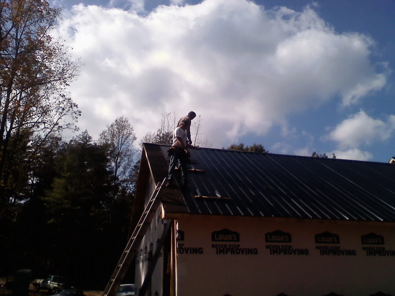 Roofer fastening dark metal panels high against a cloudy sky, from a Roof Inspection job in Mount Braddock