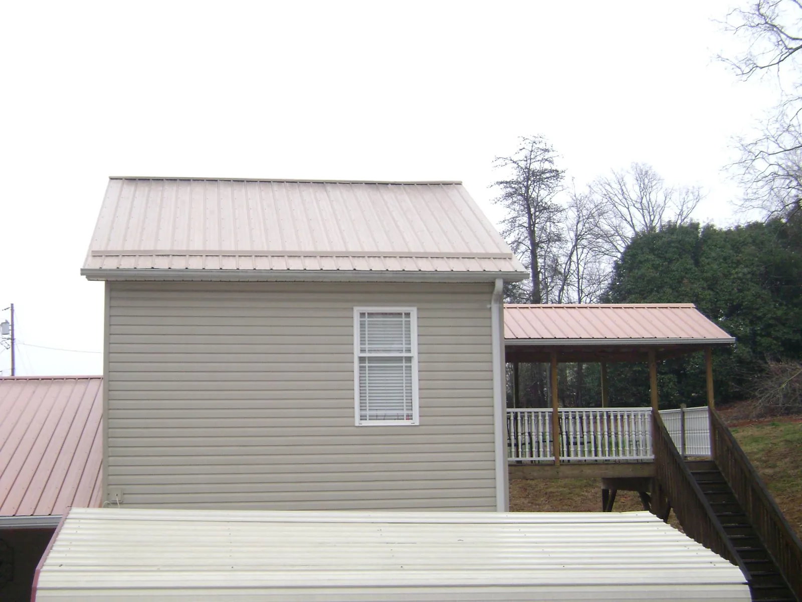 Tan metal roofs on a two story addition and attached porch, from a Roof Replacement job in Mount Braddock